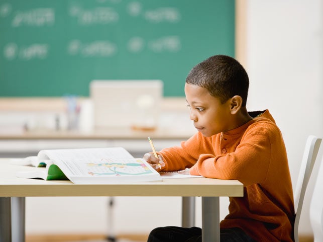 Young boy in orange shirt writing at his desk in classroom