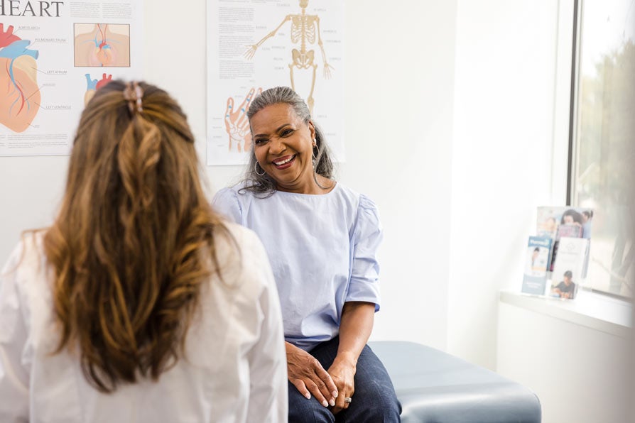 older woman sitting on exam table smiling at doctor