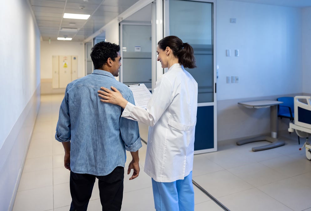 view from behind: man and doctor walking in a hospital hallway talking