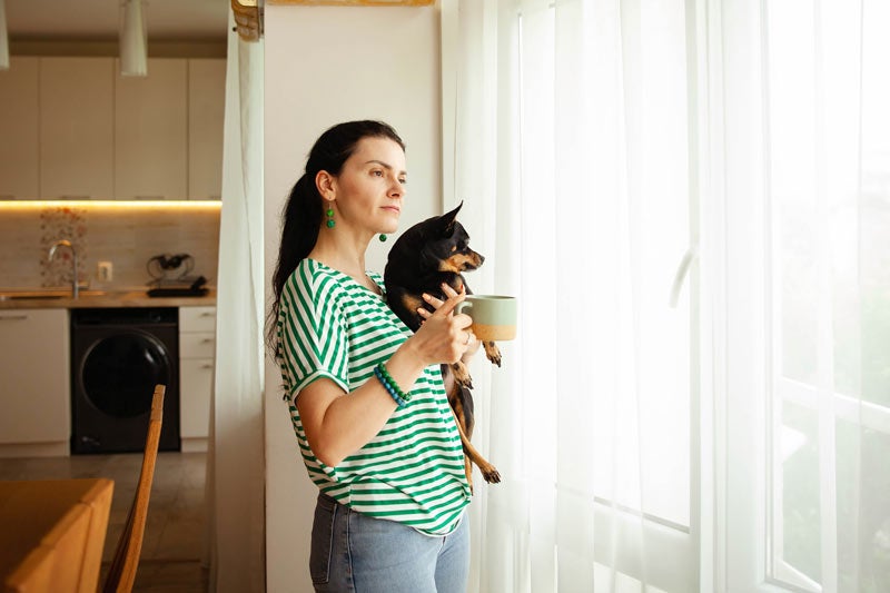Woman holding dog and looking out window
