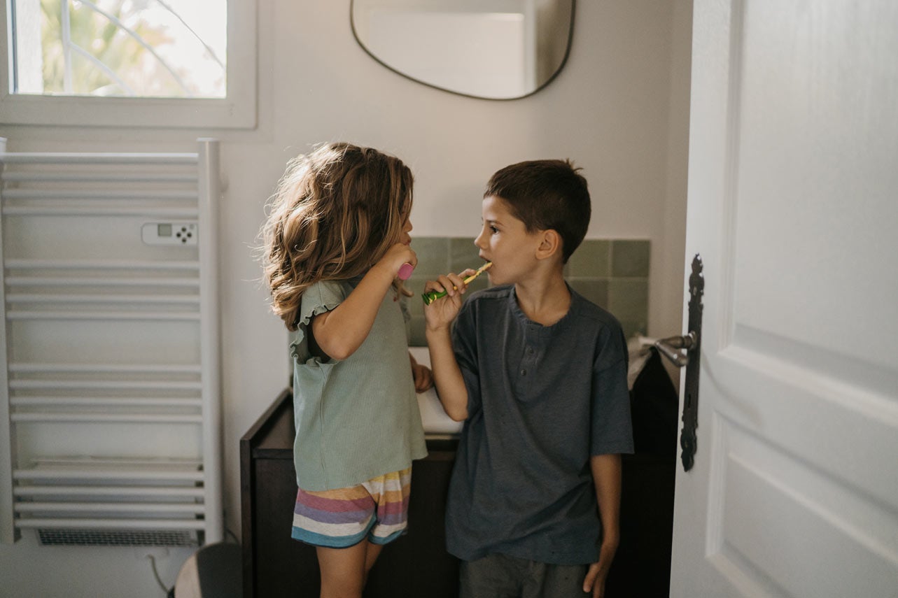 Siblings facing each other while brushing teeth in bathroom