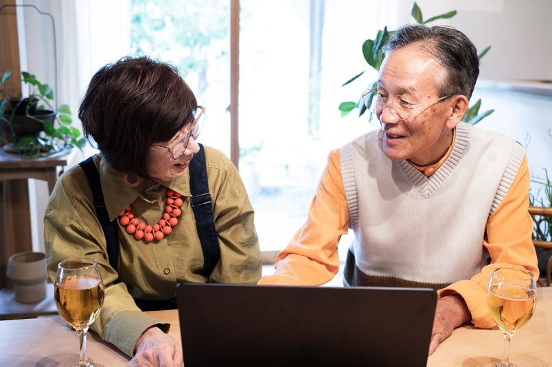 A senior couple chatting at the dining table together, looking at their laptop