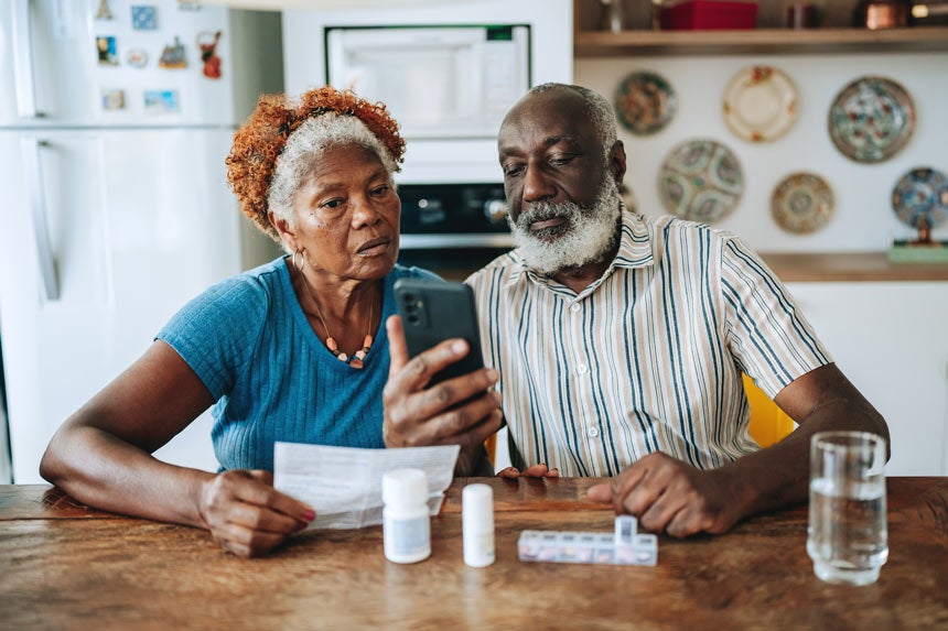 Older couple looking at phone and paper bills at table