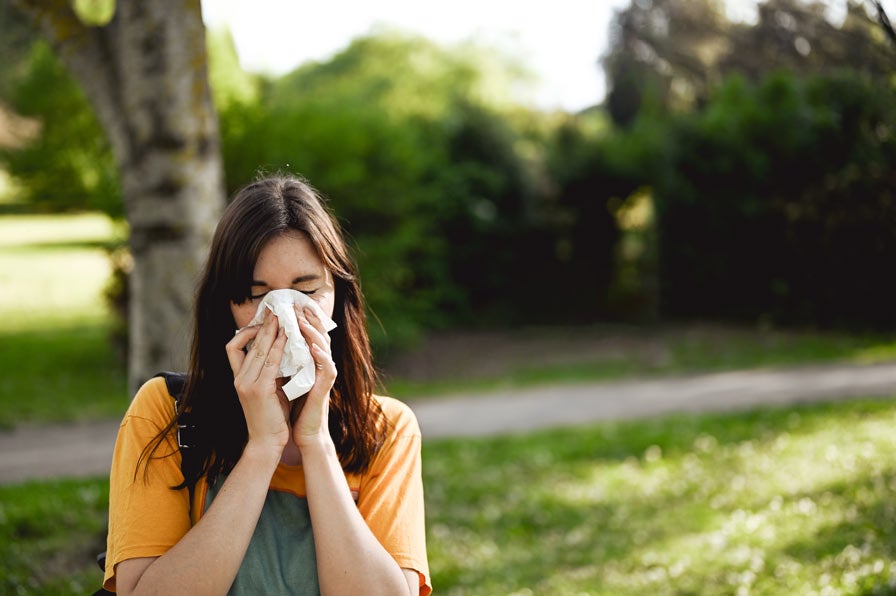Woman wiping nose with tissue outside